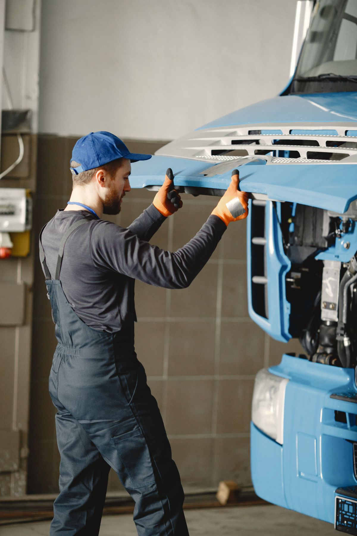 A technician fitting the front grille panel of a blue HGV cab in a service workshop